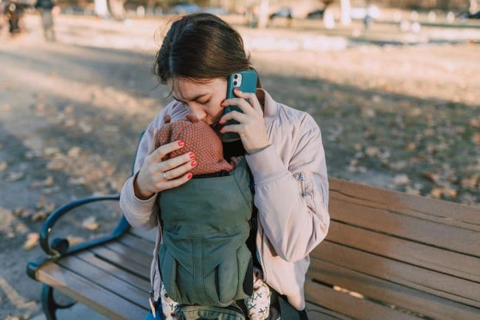 A mother holds her phone while cradling her baby
